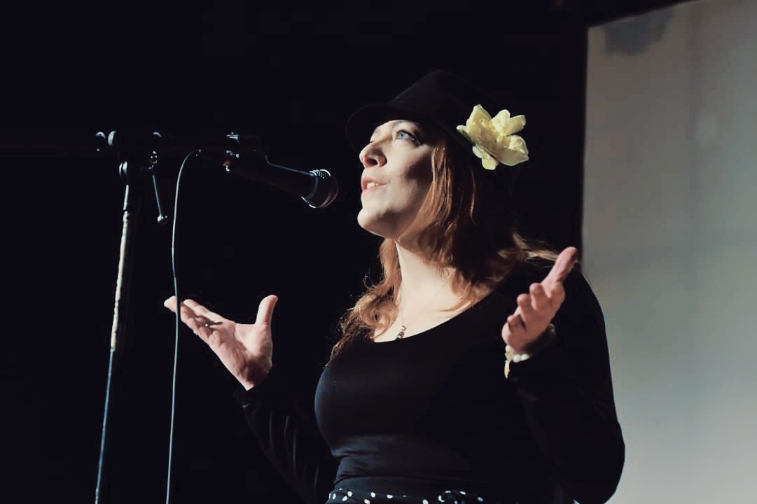 maria de los angeles with open arms wearing black at live storytelling event